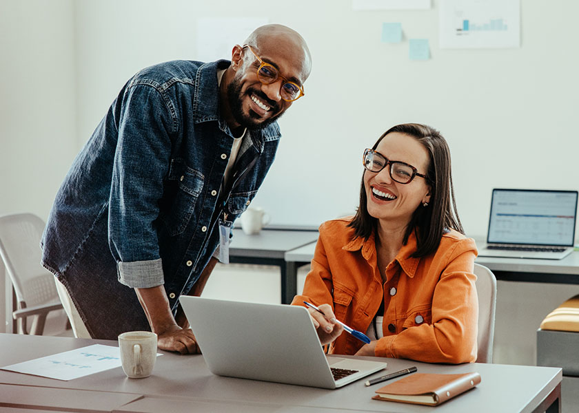 Team of smiling coworkers working together on a laptop in a bright, modern office setting, demonstrating teamwork and collaboration.